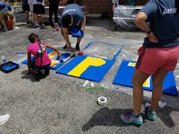 volunteers sit on the ground to paint brightly-colored letters for a sign during the 2017 Chicago Cares Serve-a-thon