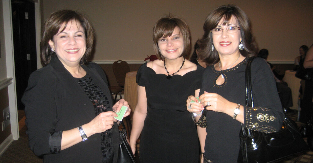 a group of three smiling women in black dresses at a Christmas party in 2008