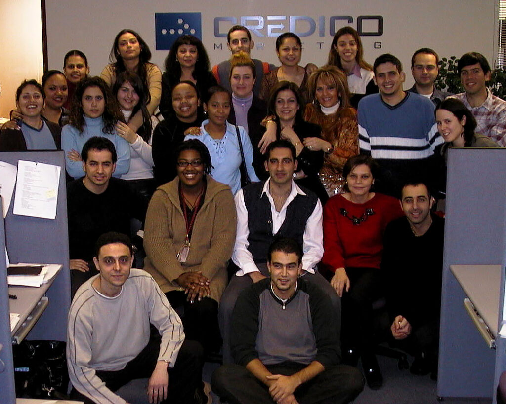 A group of people pose in a group at the end of a row of office cubicles in 2002