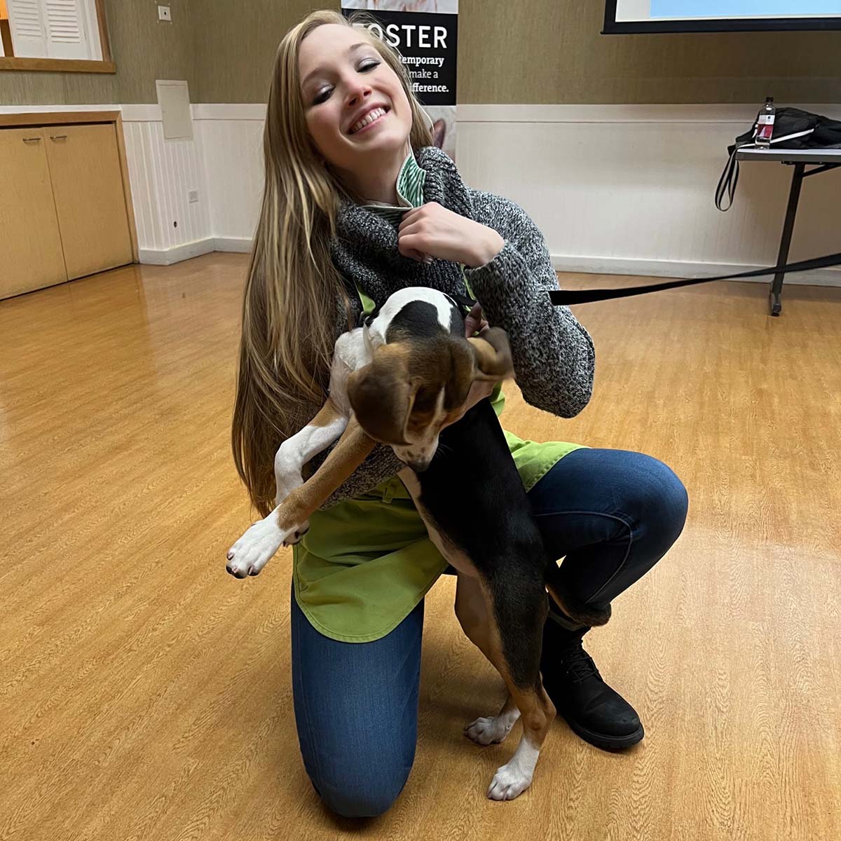 Jessica Hucek kneels on the floor smiling with an excited puppy