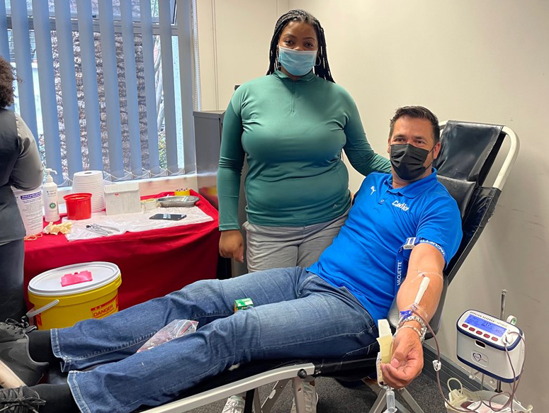 Credico South Africa's General Manager, Theuns Bezuidenhout, holds his arm outstretched while connected to blood donation equipment as a SANBS staffer looks on