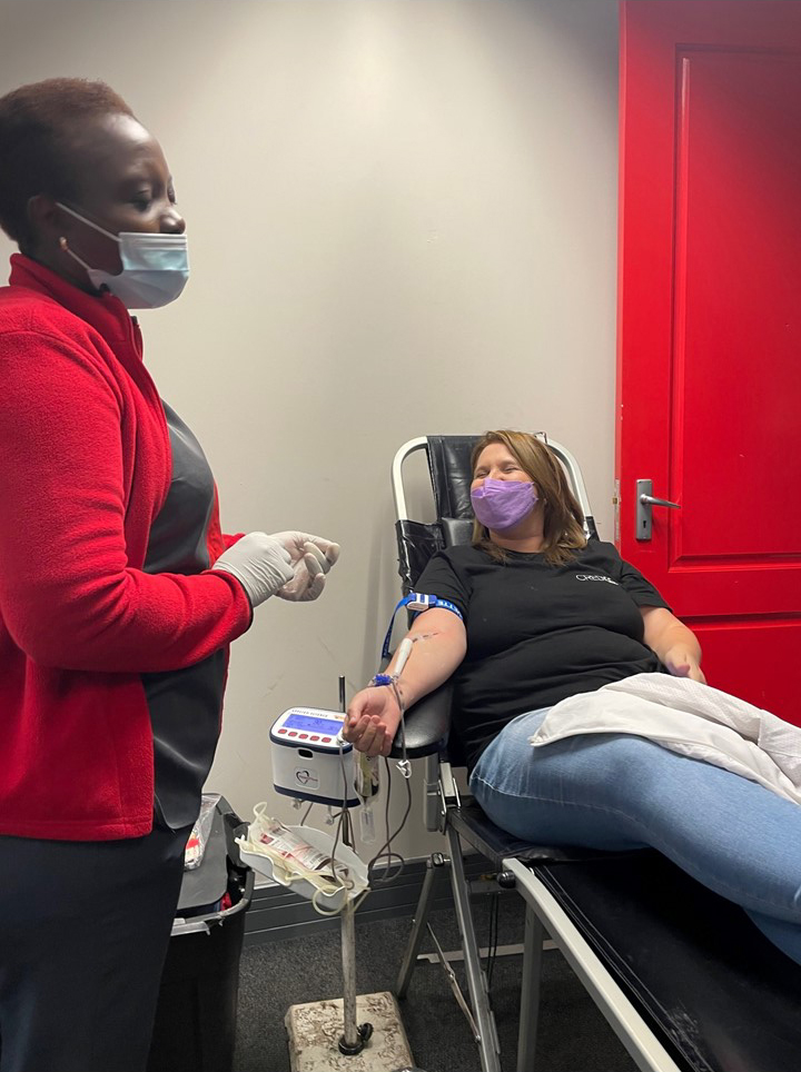 A Credico South Africa staff member reclines while donating blood and looking up at an attending SANBS worker monitoring her donation