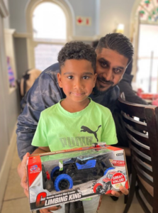 A Credico SA staff member smiles behind his son, who is holding up his Christmas in July gift of a remote control car