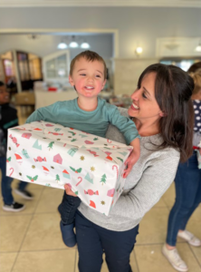 A mother holds her smiling son with a large wrapped gift during Credico SA's 2022 Christmas in July event