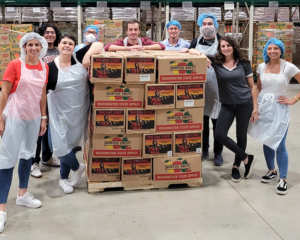 A group of volunteers from Credico USA poses smiling in front of a pallet of apples after a volunteer shift at the Greater Chicago Food Depository