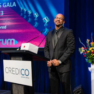 Jason Ward, wearing a black suit and shirt, smiles on stage behind a podium following his recognition as a Regional Consultant at the January 2023 North American Awards Gala in Miami, Florida