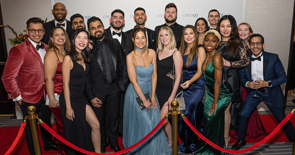 A group of attendees dressed in glittering formalwear pose for a photo on the red carpet at the January 2023 North American Awards Gala in Miami, Florida