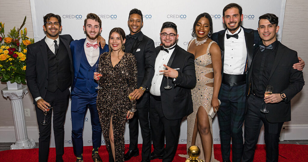 A group of attendees dressed in glittering formalwear pose for a photo on the red carpet the January 2023 North American Awards Gala in Miami, Florida