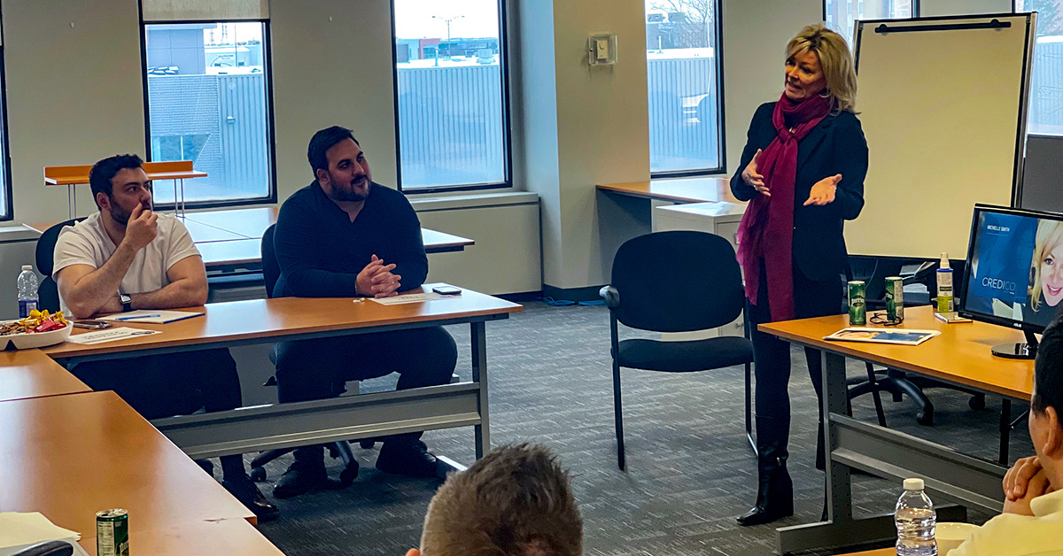 Michelle Smith leads a meeting of Canadian and US Credico employees in a conference room in front of a whiteboard.