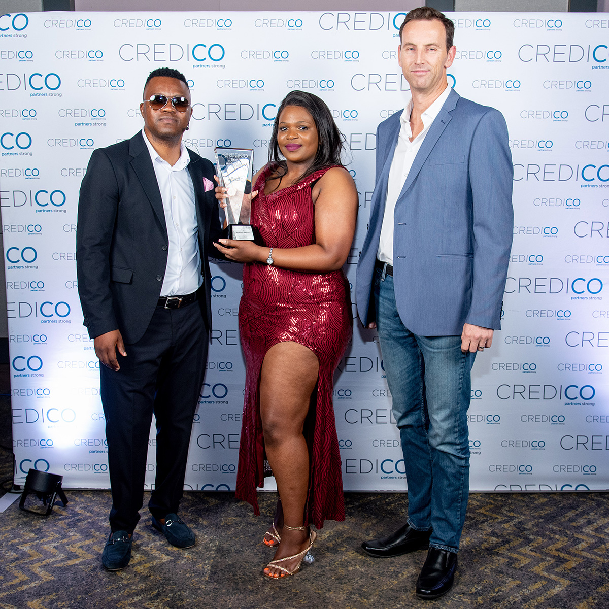 A winner poses with her award and two companions in front of a branded background at Credico South Africa's 2023 Awards Gala at Sun City Resort.