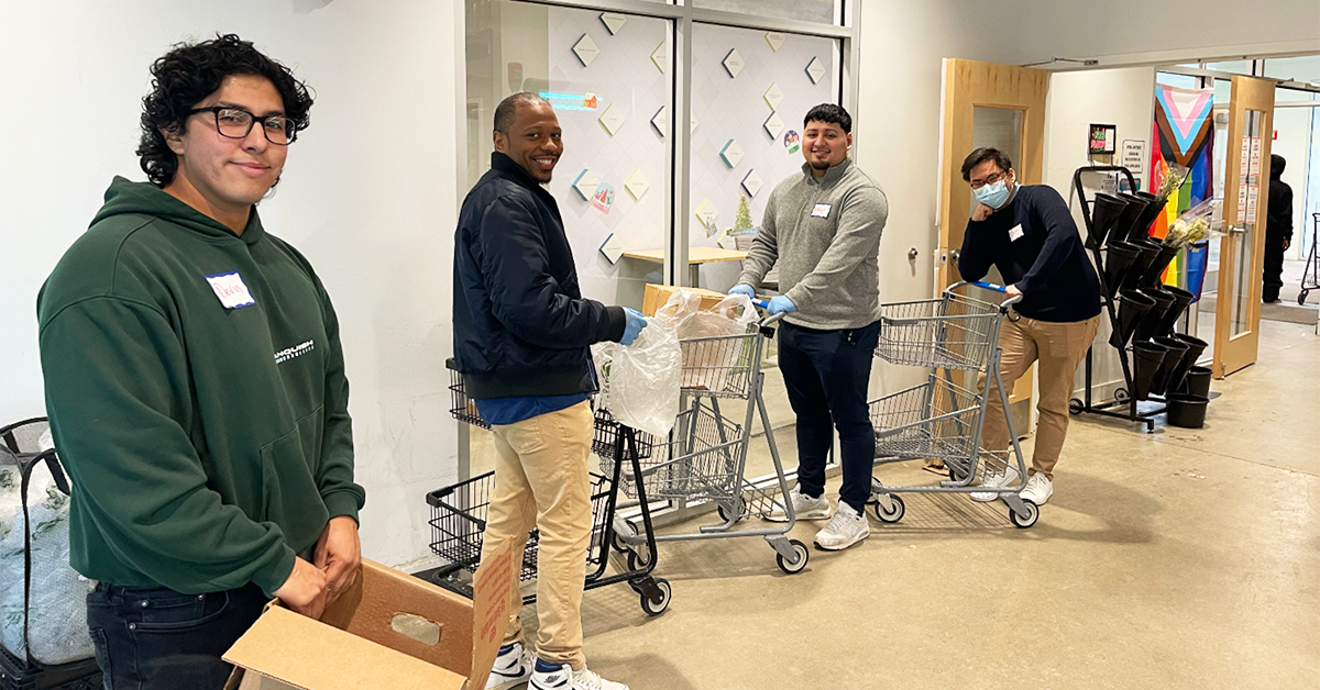 four volunteers from Credico (USA) LLC's Legal and Onboarding departments stand in the hallway of El Mercadito with shopping carts while donating their time to Nourishing Hope's mission of reducing food insecurity in Chicago.