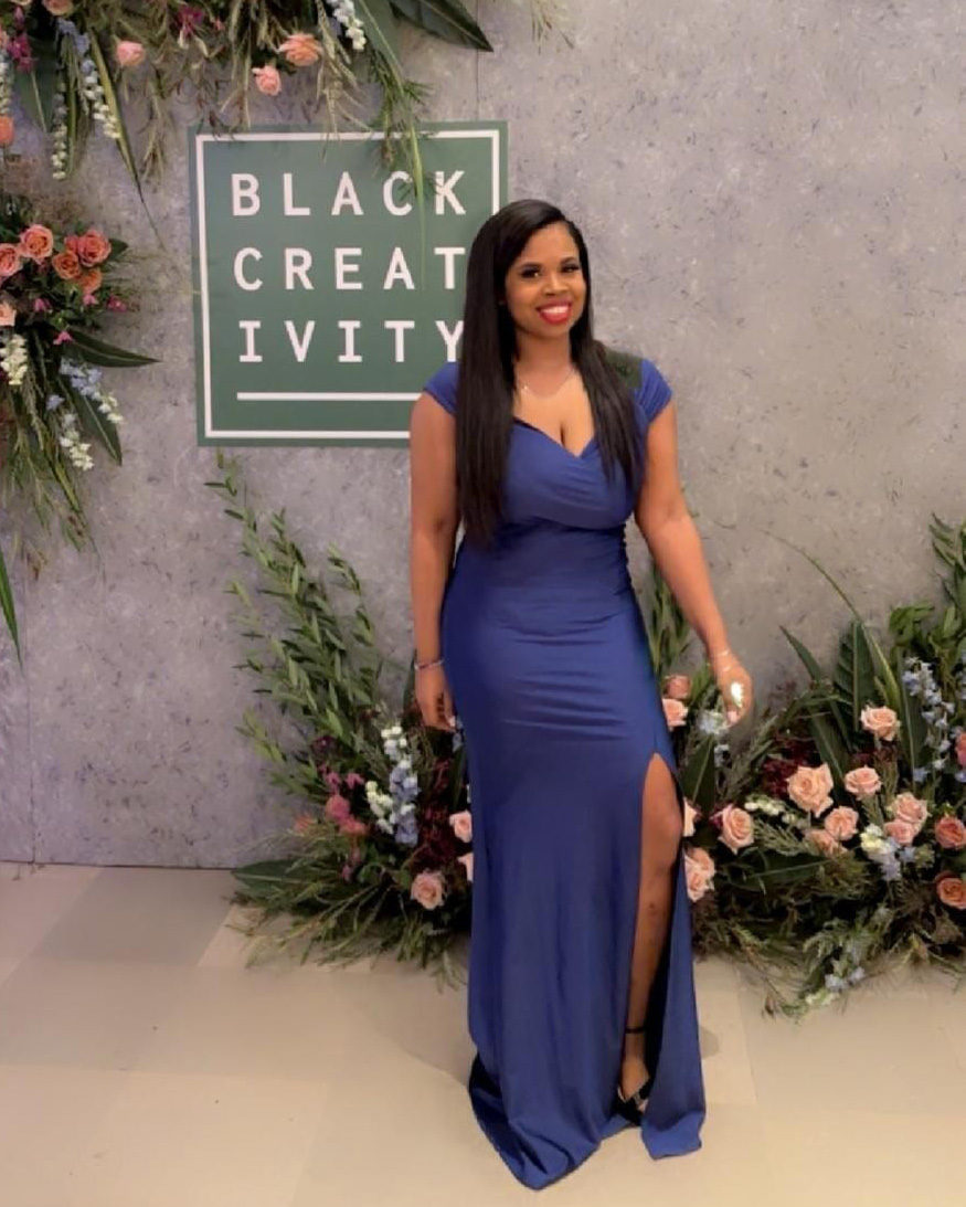 Brittany Cross, Human Resources Business Partner at Credico (USA) LLC, poses in a blue formal gown in front of the Black Creativity sign at the 2024 Black Creativity Gala at Chicago's Museum of Science and Industry