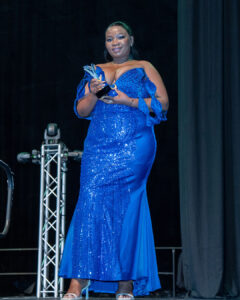 An award winner poses with her trophy in a sparkling blue ball gown on stage at the South Africa Awards Gala in March 2025