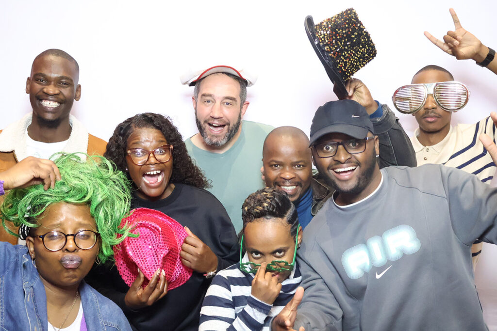 a group of excited people pose in a photobooth with hats and wigs at Credico South Africa's 2025 Christmas in July
